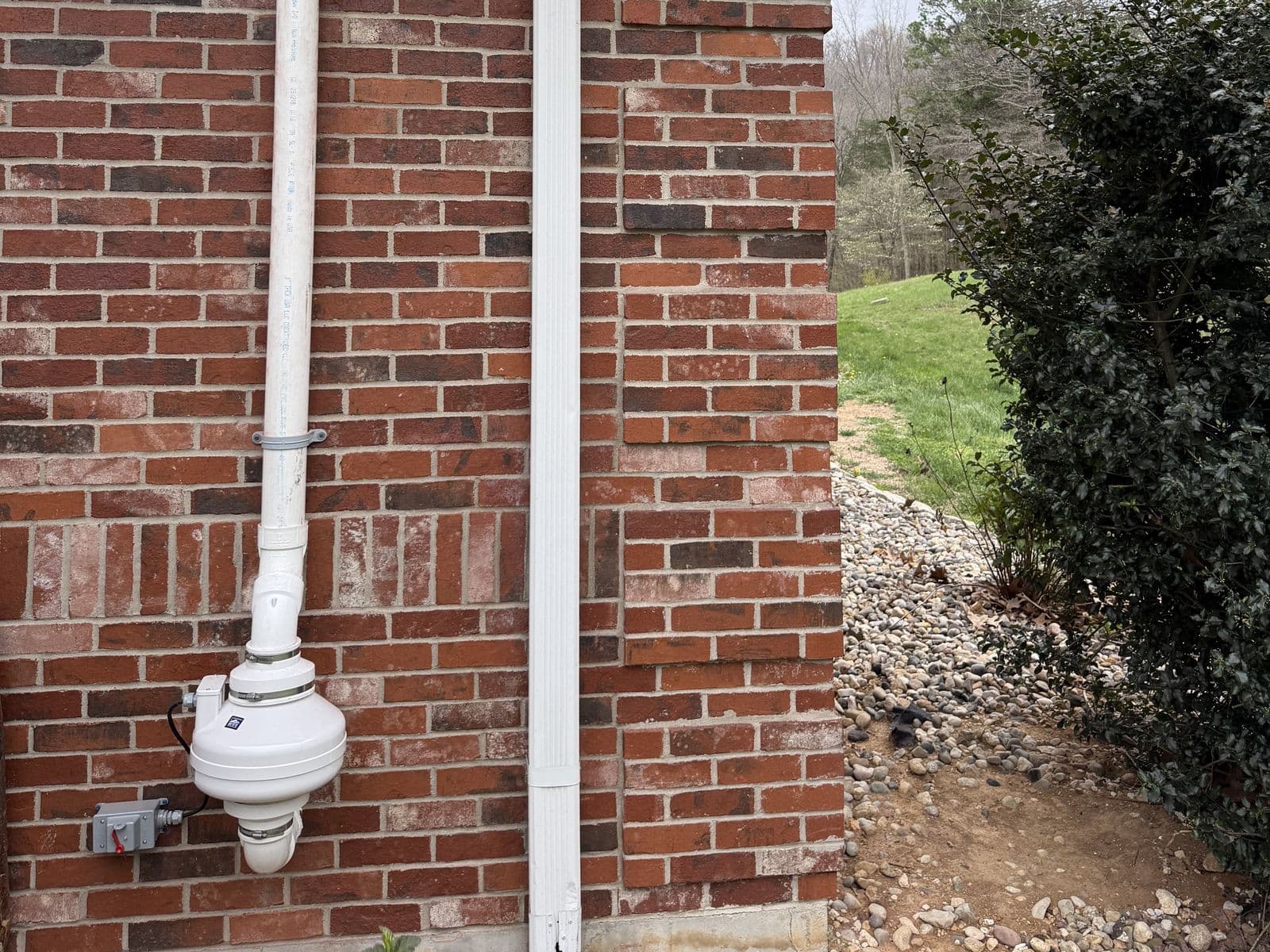 Radon mitigation system installed by Eagle Air on a brick home, with the radon fan and white PVC vent pipe running up the outside wall